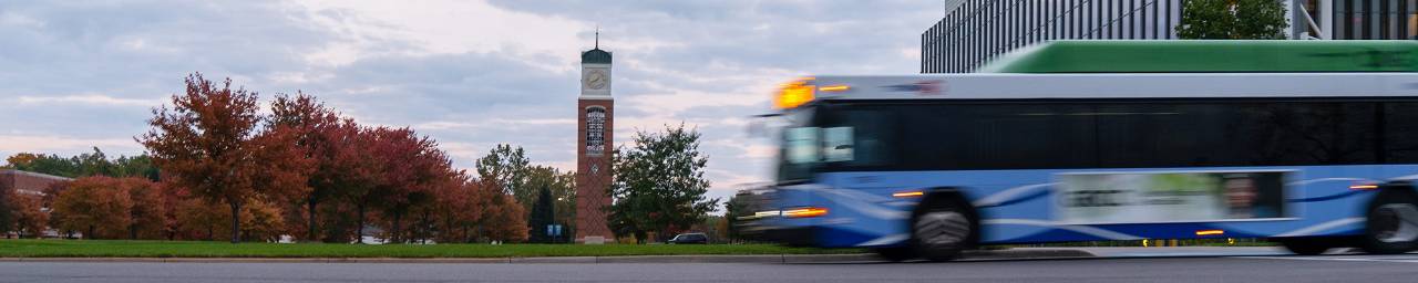 A Hybrid style rapid bus driving past the Cook Carillon Clock Tower on GVSU's Allendale Campus